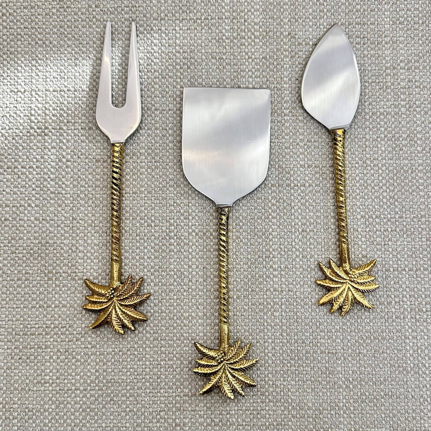 Set of three metal dessert spoons with leaf designs on a textured gray background