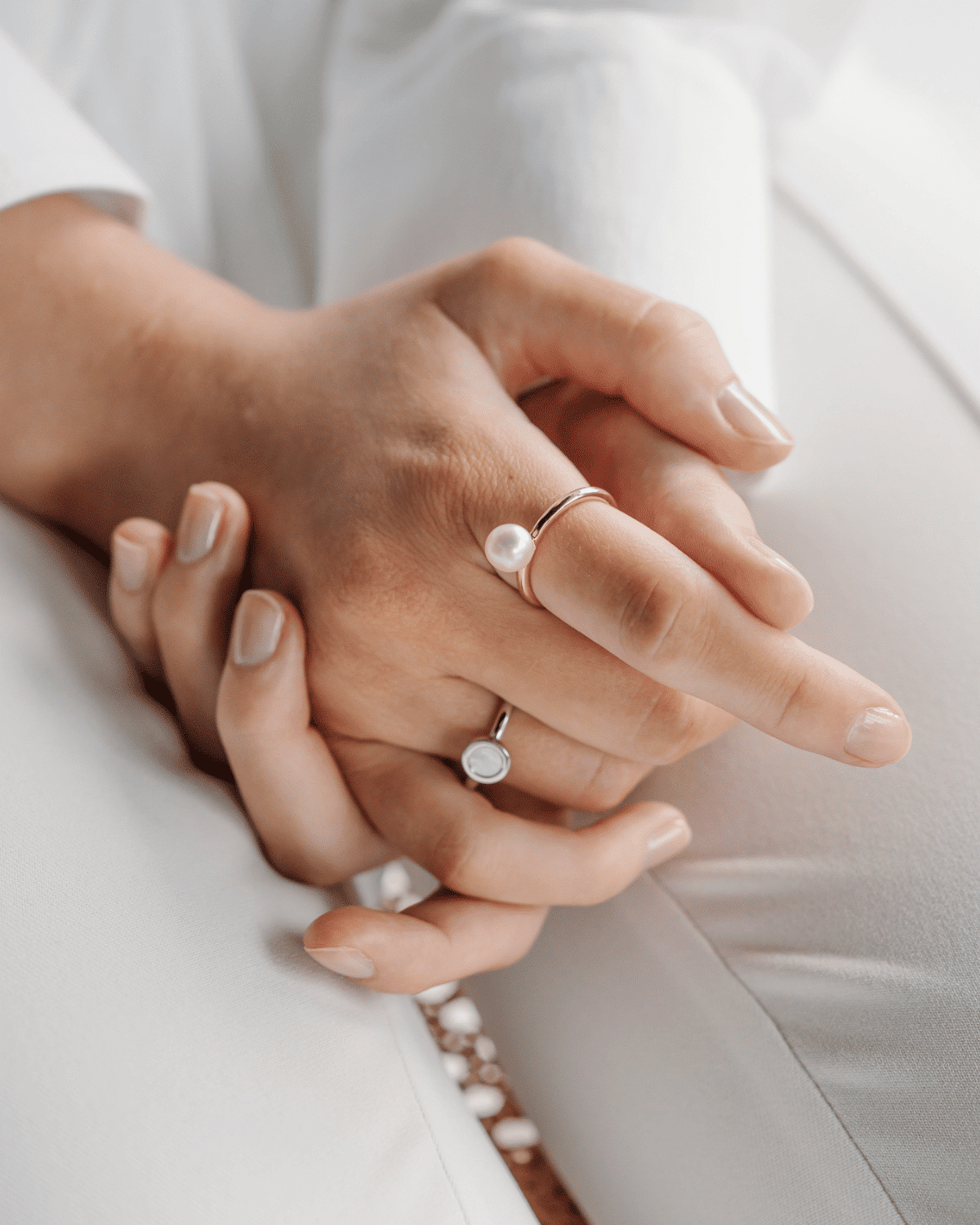 A person a rests their hands on their lap, while wearing their stunning pearl ring featuring an Akoya pearl on one finger, and a Mother of pearl ring featuring our Cygnet Bay grown Mother of Pearl shell on another finger.