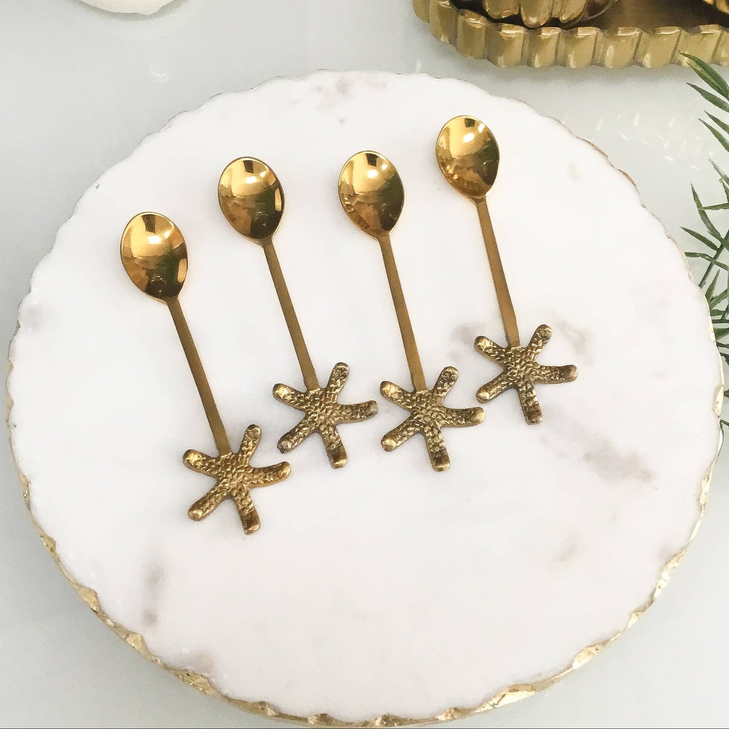 Set of gold star-shaped spoons on a white plate with decorative items in the background.