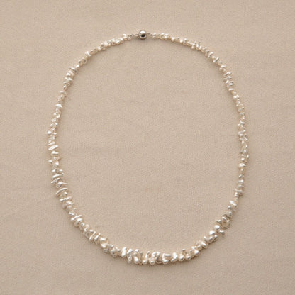 A delicate pearl strand necklace made of irregular white Keshi pearls arranged in a circle, displayed on a neutral beige background.