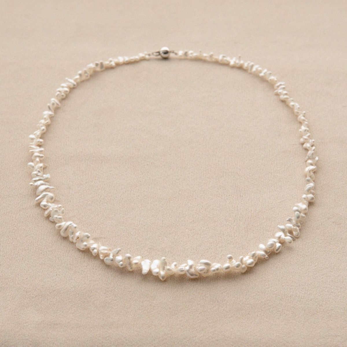A delicate necklace made of irregular white Cygnet Bay grown Keshi pearls with an 18ct white gold clasp, displayed on a neutral beige background.