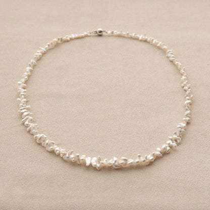 A delicate necklace made of irregular white Cygnet Bay grown Keshi pearls with an 18ct white gold clasp, displayed on a neutral beige background.