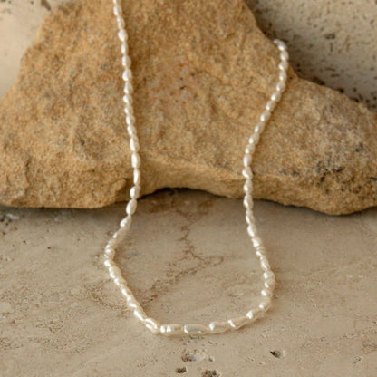 A delicate white Keshi pearl strand necklace draped over a natural tan rock on a textured stone surface.