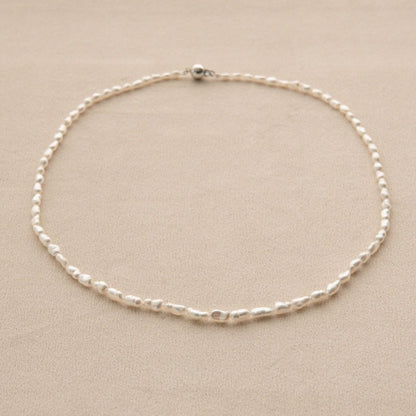 A delicate pearl strand necklace with irregular, organic shaped Keshi pearls arranged in a circle on a neutral beige background.