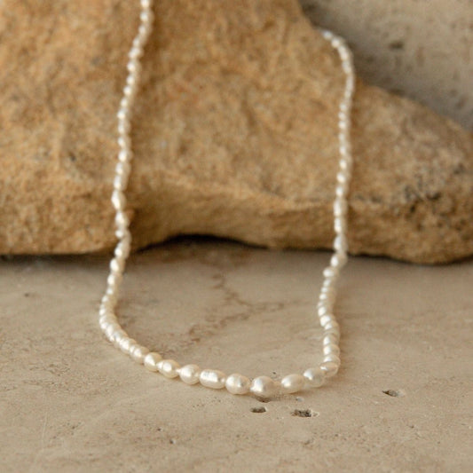 A strand of irregular white Keshi pearls draped over a tan stone on a textured beige surface.