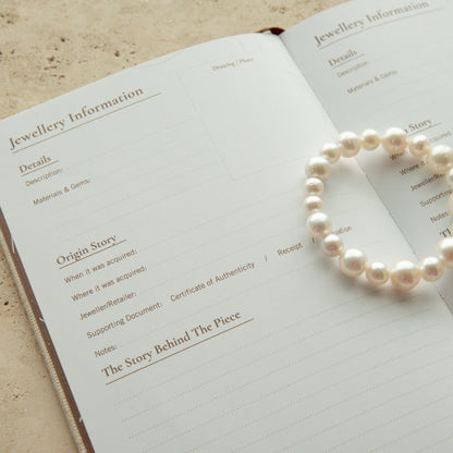 An open lined journal or notebook on a textured beige surface, with an  Australian South Sea pearl strand bracelet draped over the pages.