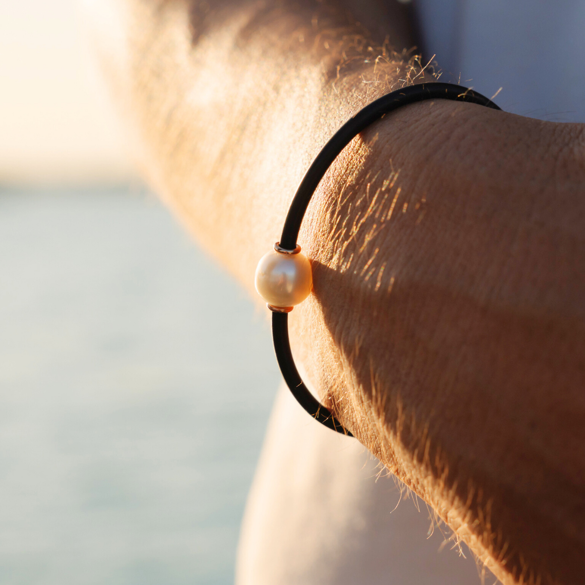 Close-up of a wrist wearing a neoprene pearl bracelet against a blurred natural background