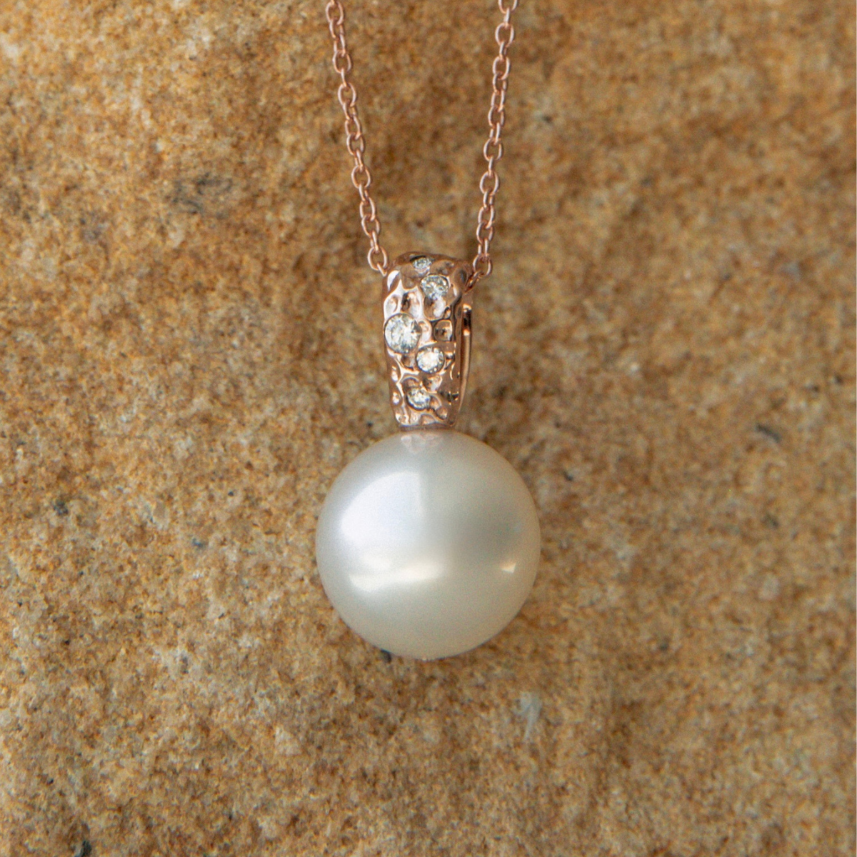 Pearl necklace with rose gold clasp on a textured brown background