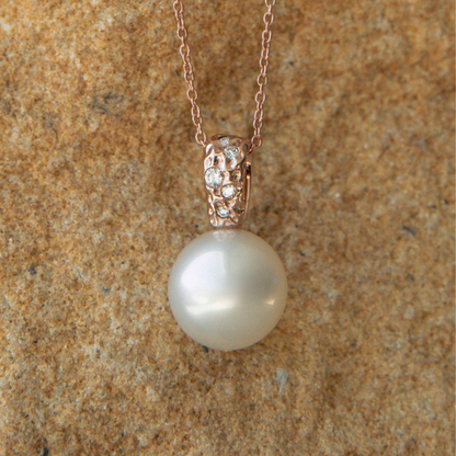 Pearl necklace with rose gold clasp on a textured brown background