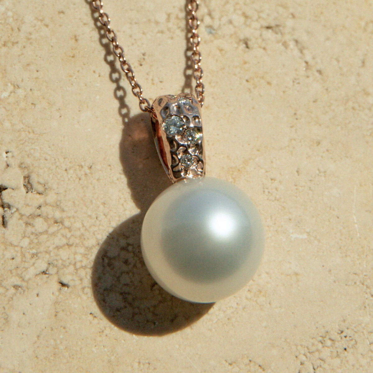 Pearl necklace with rose gold chain on a sandy background