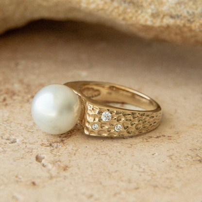Gold ring with a pearl and small diamonds on a sandy background