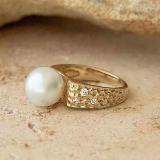 Gold ring with a pearl and small diamonds on a sandy background