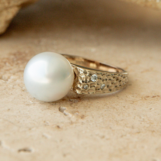 Gold ring with a large pearl and smaller stones on a beige background