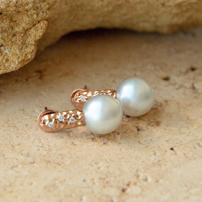 Pearl earrings with rose gold clasps on a sandy surface
