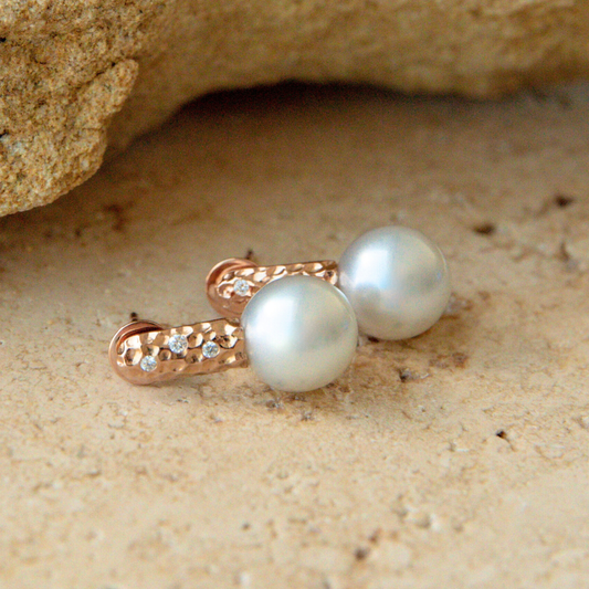 Pearl earrings with rose gold clasps on a sandy surface