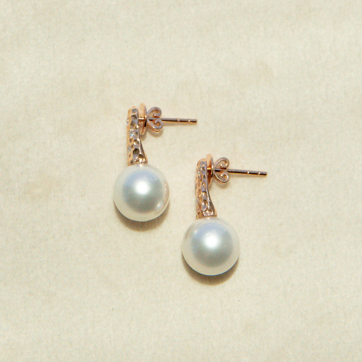 Pearl earrings with rose gold accents on a beige background