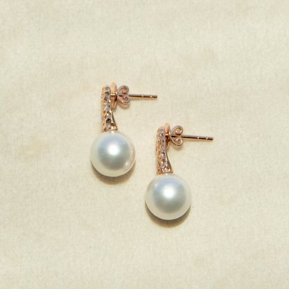 Pearl earrings with rose gold accents on a beige background