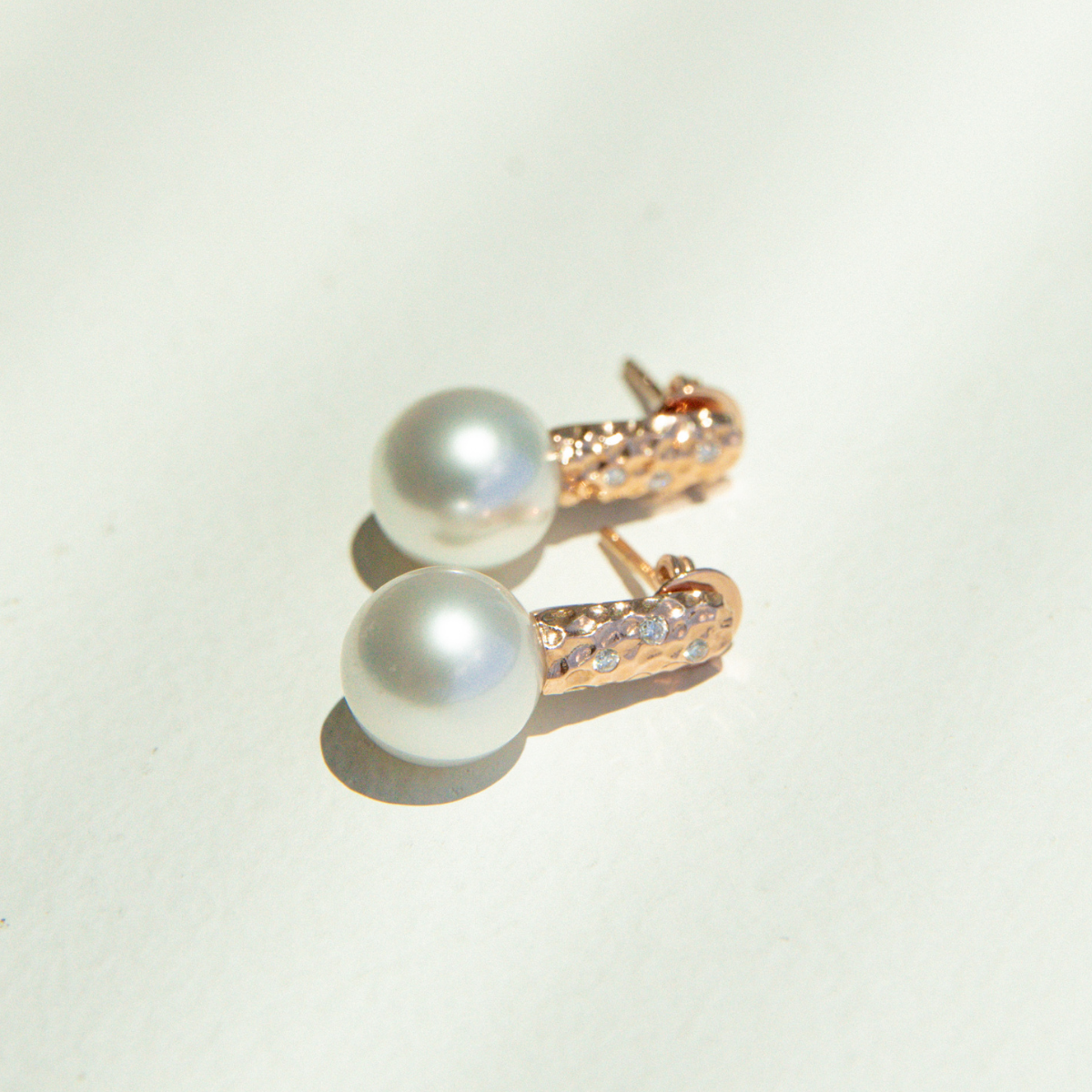 Pearl earrings with rose gold clasps on a light background