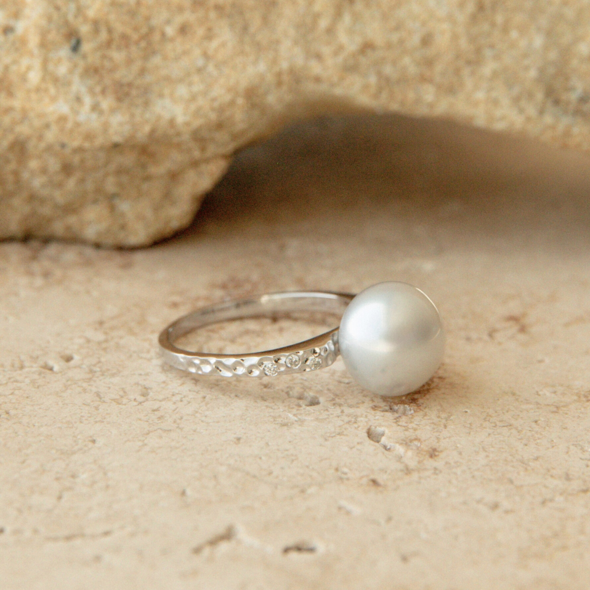 White gold ring with a pearl on sandy surface