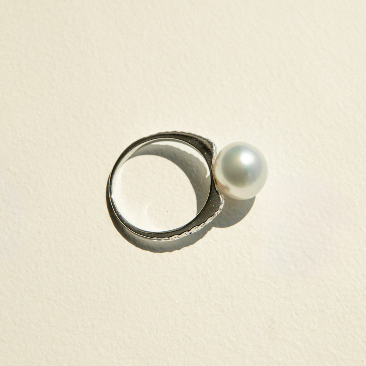 White gold ring with a pearl on a beige background