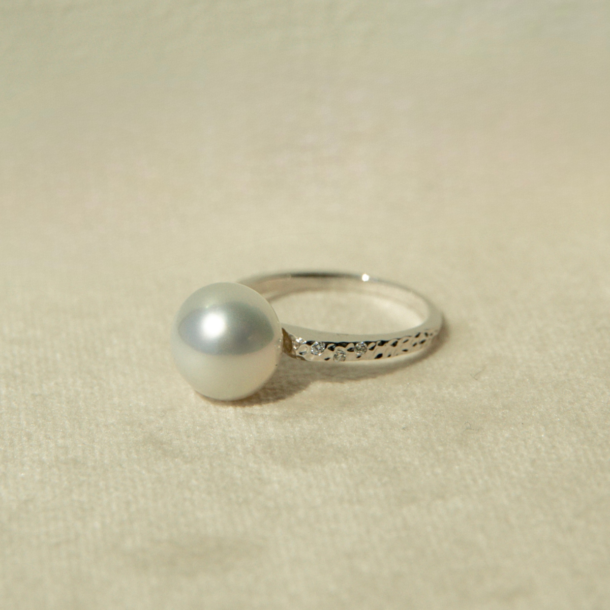 White gold ring with a pearl on a beige fabric background