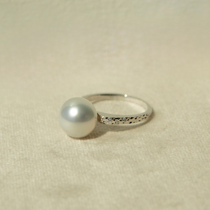 White gold ring with a pearl on a beige fabric background