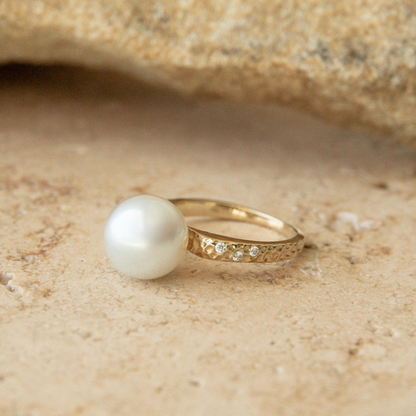 Gold ring with a pearl on a sandy background