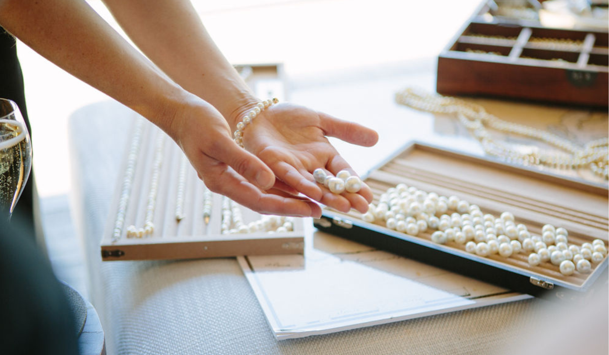 Person handling pearls with a jewellery display tray and necklace on a table