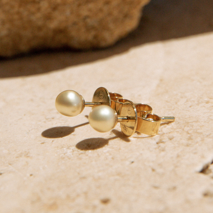 Gold keshi pearl earrings on a sandy surface