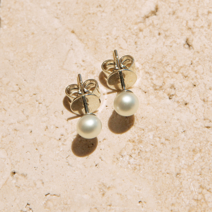 Pair of keshi pearl stud earrings on a beige textured surface