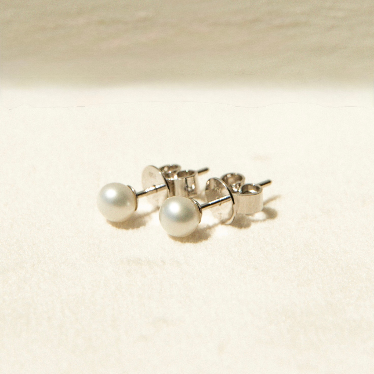 Pair of keshi pearl stud earrings on a beige background