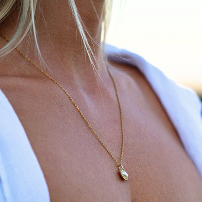 A woman wears her unique Kimberley Lily Petite Pendant featuring an Australian South Sea Keshi pearl set in a unique lily inspired design in yellow gold.