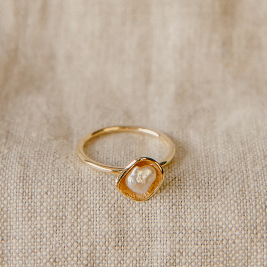 Gold ring with a central keshi pearl on a beige fabric background