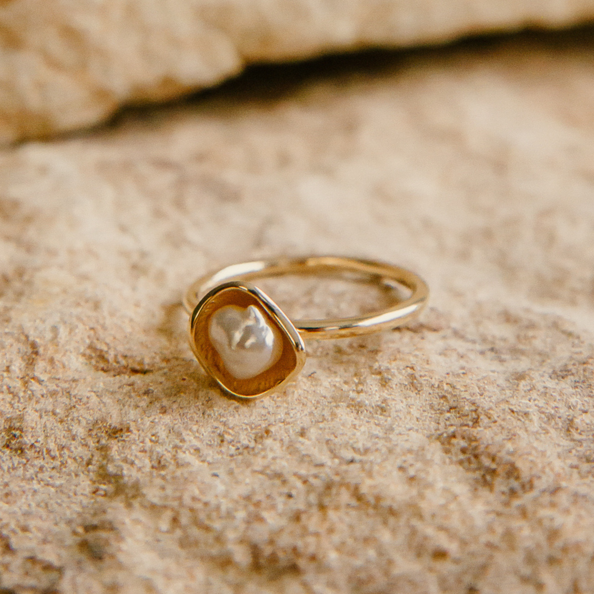 Gold ring with a keshi pearl on a textured beige surface