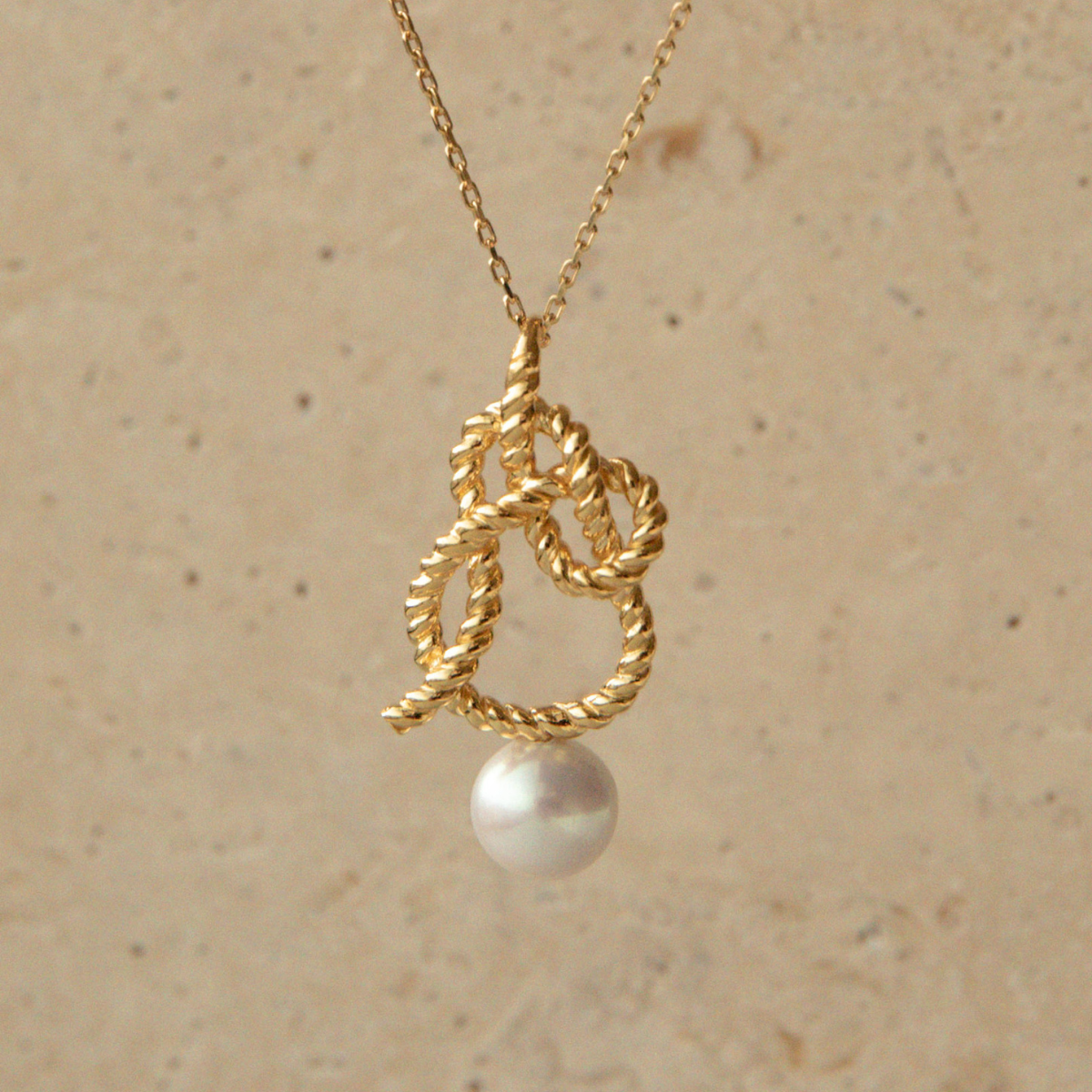 Gold necklace with a pearl pendant on a beige background