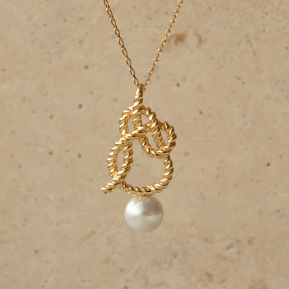Gold necklace with a pearl pendant on a beige background