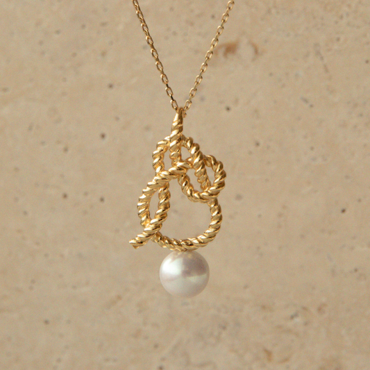 Gold necklace with a pearl pendant on a beige background