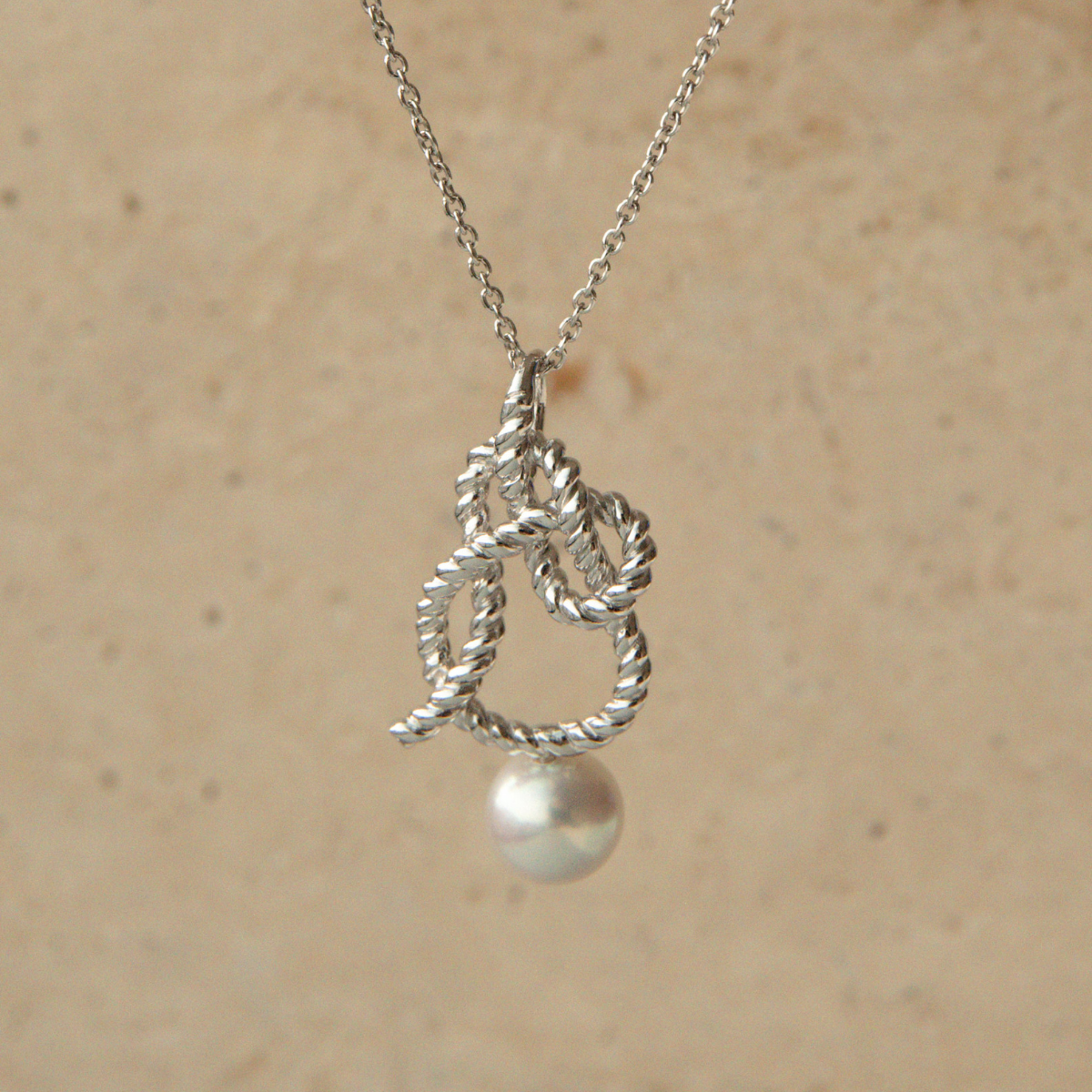 Silver knot pendant with a pearl on a beige background