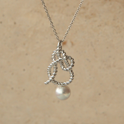 Silver knot pendant with a pearl on a beige background