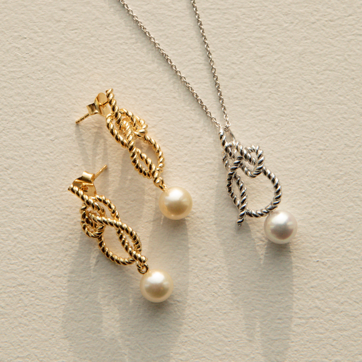 Gold pearl earrings and matching pearl pendant on a light background