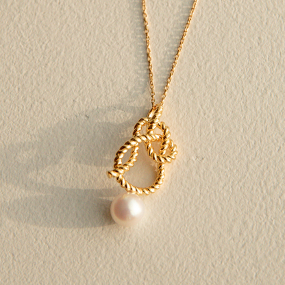 Gold necklace with a pearl pendant on a beige background
