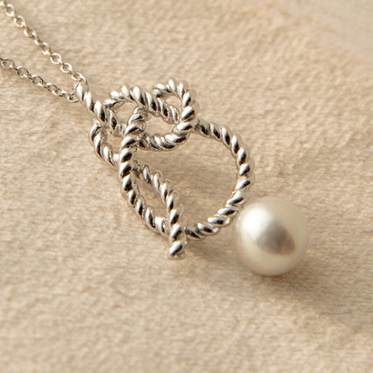 Silver necklace with twisted design and pearl pendant on beige fabric background