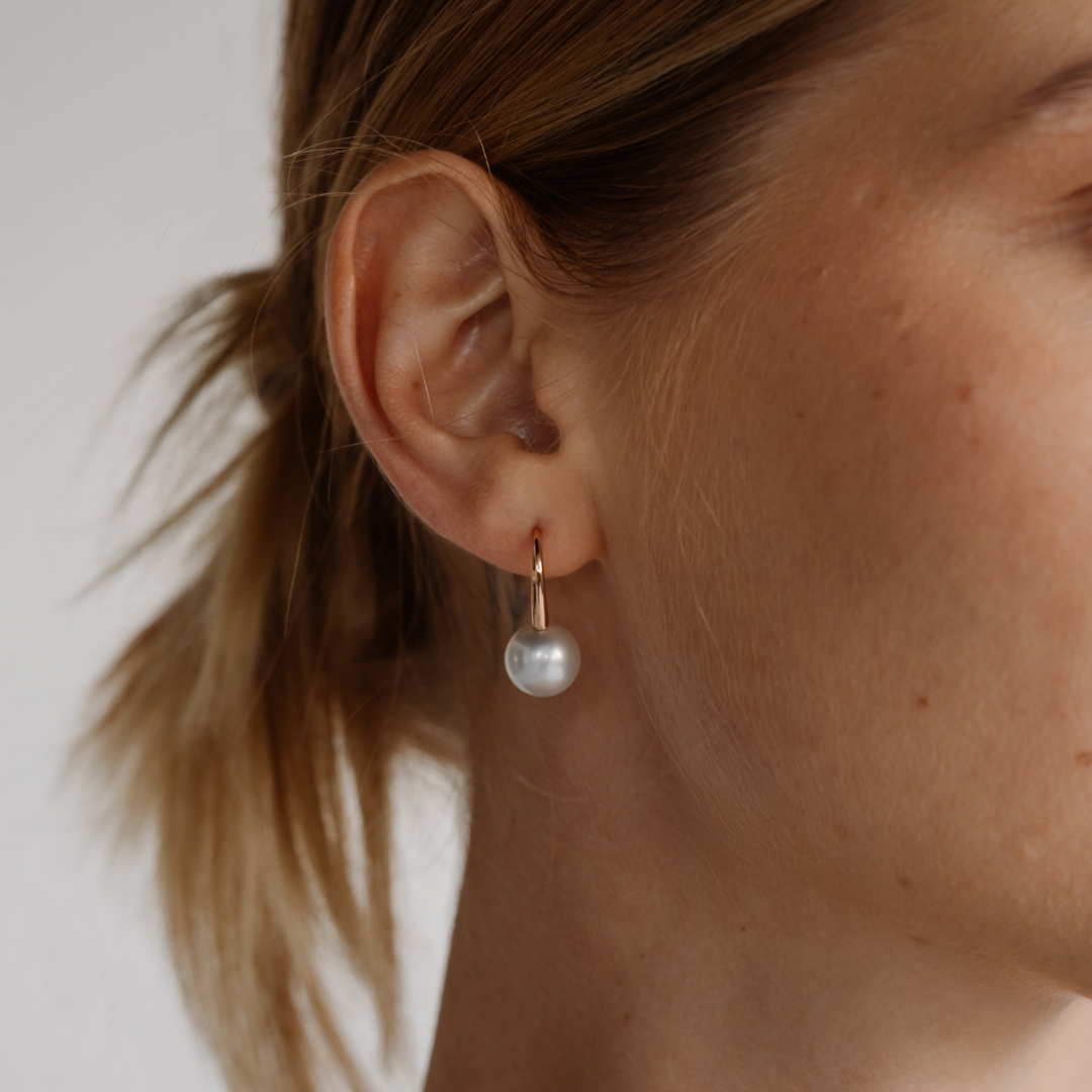 A woman wears a classic pair of Liquid Pearl Hook Earrings featuring a pair of Cygnet Bay (WA) grown Australian South Sea pearls set in gold.