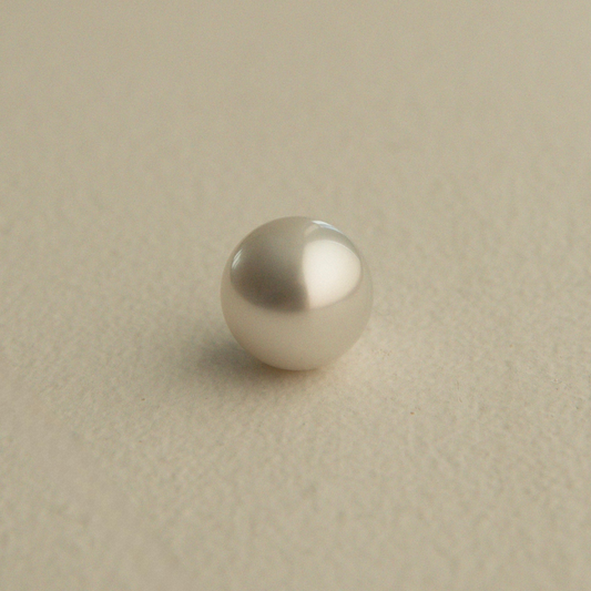 A single round, lustrous Australian South Sea pearl with a soft champagne-silver sheen, resting on a textured beige surface.