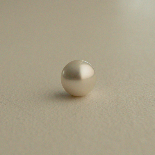 A single round Australian South Sea pearl on a textured beige background.