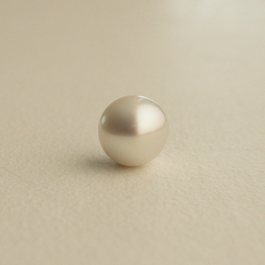A single round Australian South Sea pearl with a lustrous cream-white sheen, resting on a textured beige surface.