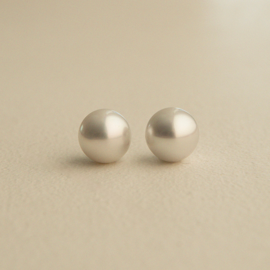 A pair of round, Australian South Sea pearls resting on a smooth, light beige surface.