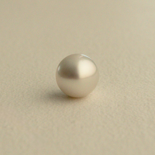 A single round Australian South Sea pearl with a soft champagne-gold sheen, resting on a textured beige surface.