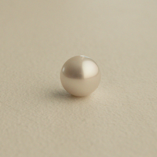 A single round Australian South Sea pearl in a warm cream or champagne color, resting on a textured beige surface.