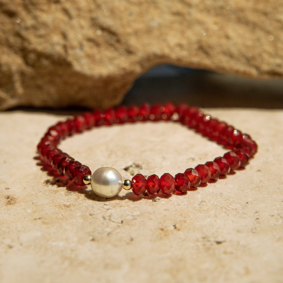 Red beaded bracelet with a pearl on a sandy surface